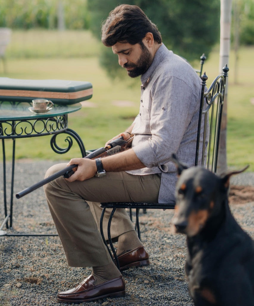 Man sitting outdoors with a doberman dog, holding a rifle.